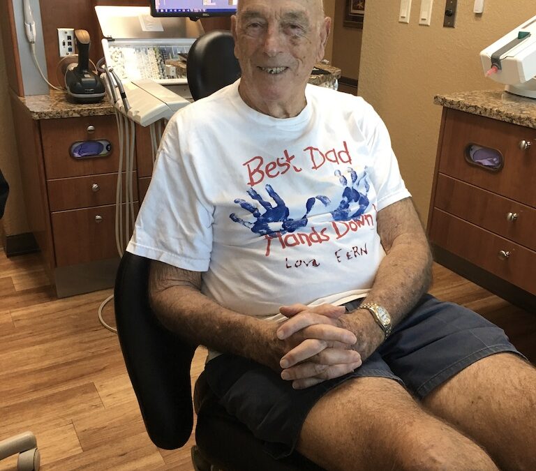 Father wearing "Best Dad, Hands Down" t-shirt, smiling in a dentist's chair.